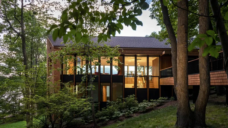 Lakeside elevation with cedar shingles and black cladding lit from within at twilight