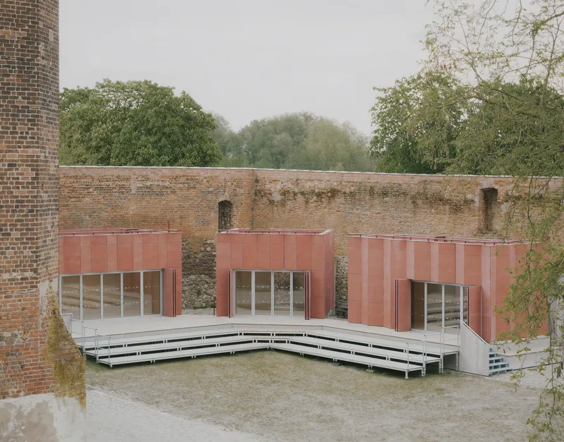 Courtyard with copper-clad pavilions set against weathered brick walls and tiered timber seating under fog