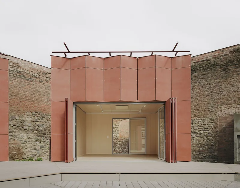 Folding glass doors open beneath a faceted copper panel canopy flanked by rough masonry walls