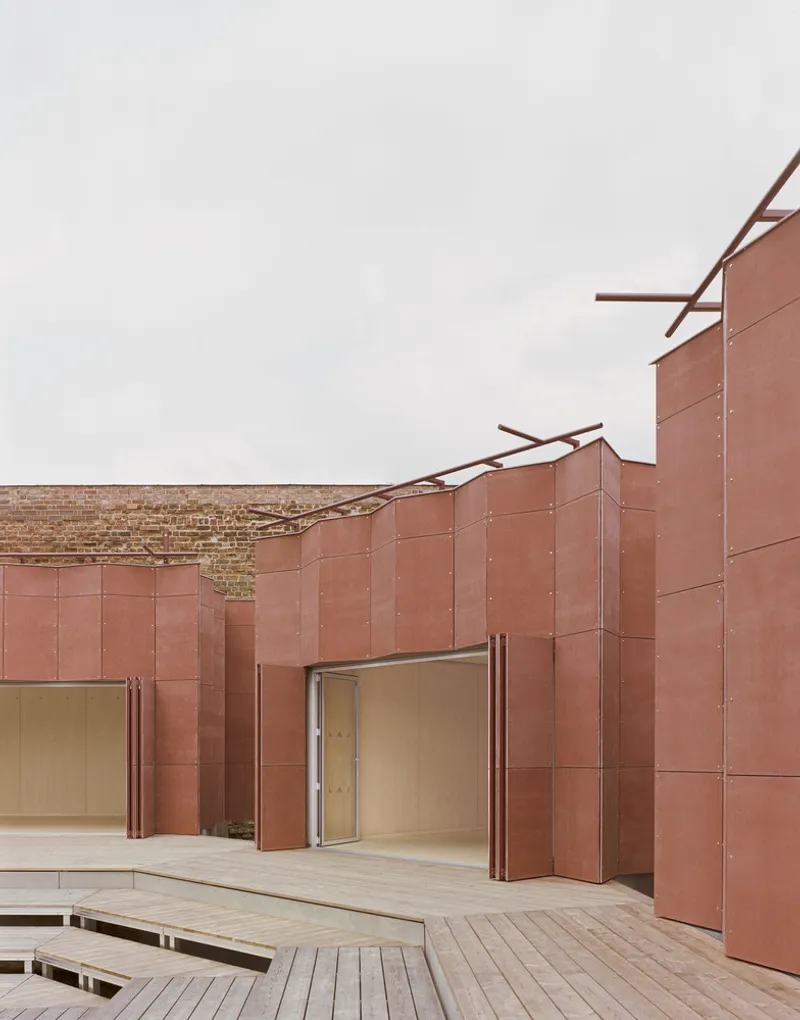 Faceted copper panel walls with angled roof braces rising above a timber deck and doorway