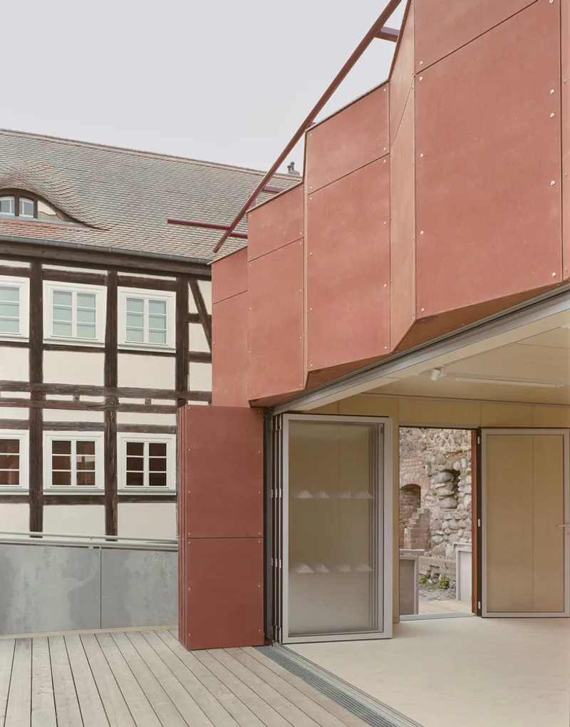 Corner detail of copper-clad volume with angled roof braces beside a timber-framed building