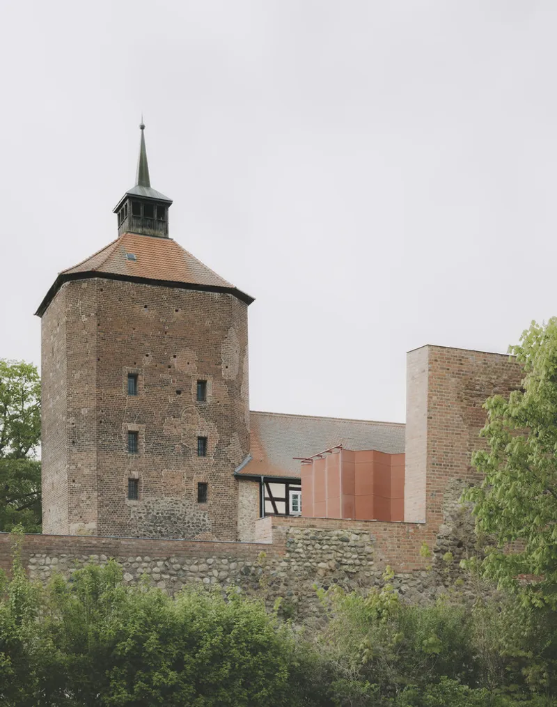 Cylindrical brick tower with green copper spire rising above stone fortification walls and copper addition