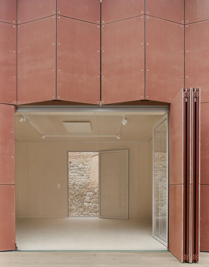 Glass entrance beneath copper cladding revealing interior gallery space with opening to stone fortress wall