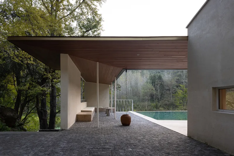 Covered terrace with timber ceiling and dark stone paving overlooking a pool and forested hillside