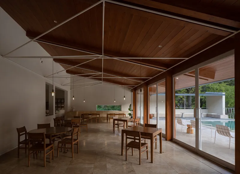 Dining hall with exposed timber ceiling trusses and full-height glazed doors opening to the pool terrace