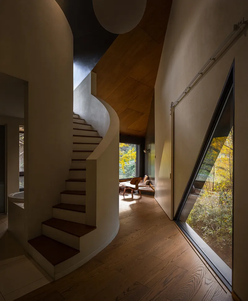 Curved staircase with timber treads beside an angled window overlooking autumn foliage