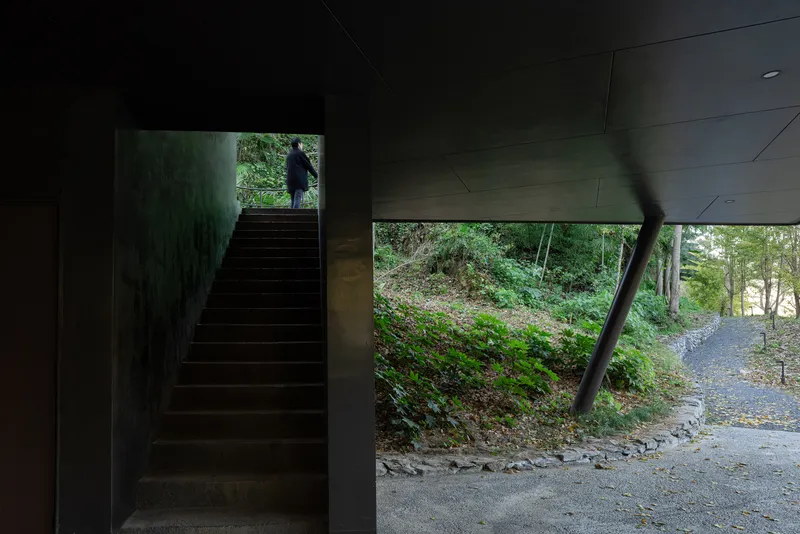 Interior staircase ascending toward daylight with figure silhouetted at the upper landing
