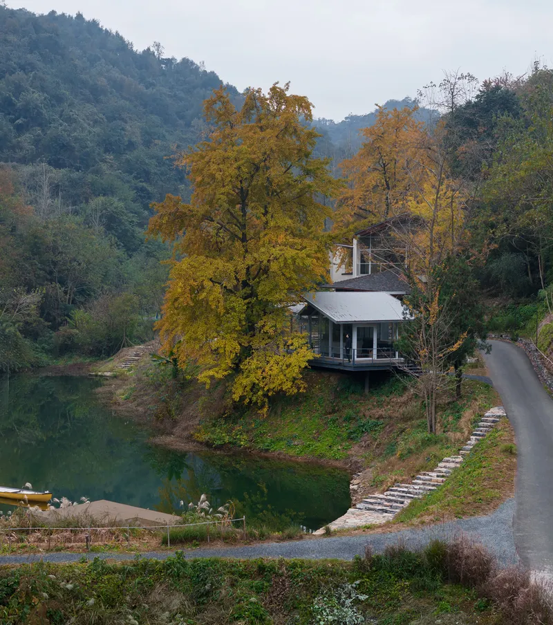 Distant view of the lakeside residence with stone pathway and yellow autumn foliage in forested hills
