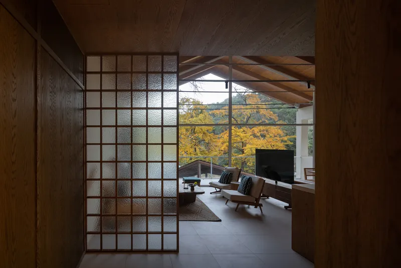 Translucent glass block sliding door opening to the living room with exposed timber ceiling and autumn trees beyond