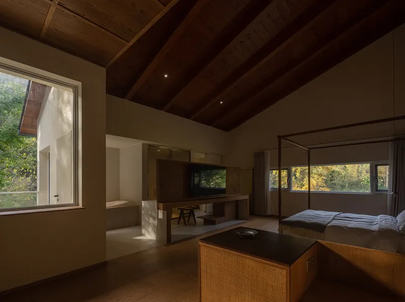 Bedroom suite with exposed timber ceiling and horizontal ribbon windows overlooking autumn trees