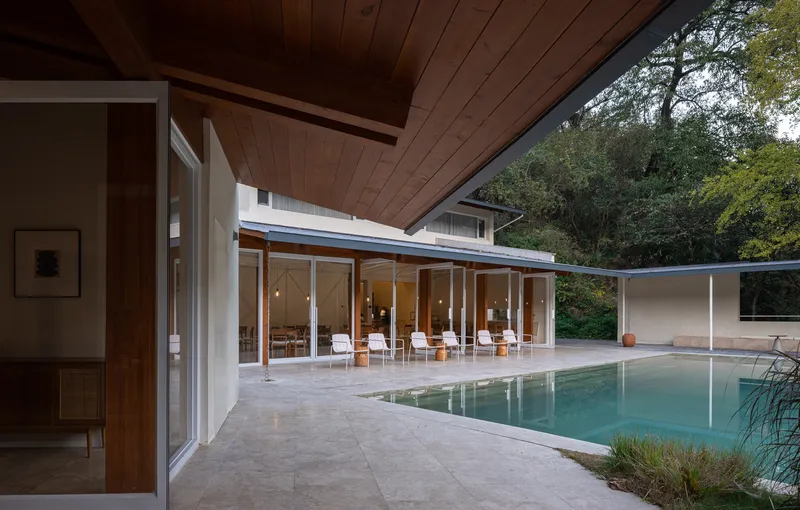 Poolside terrace with limestone paving and timber-ceilinged pavilion opening to trees at dusk