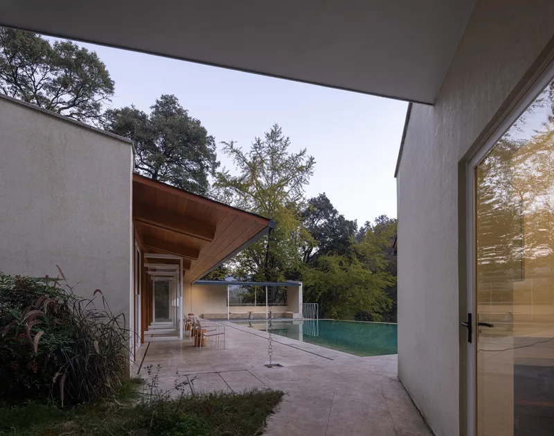 Covered walkway with concrete deck and timber soffit framing view of the pool and oak trees