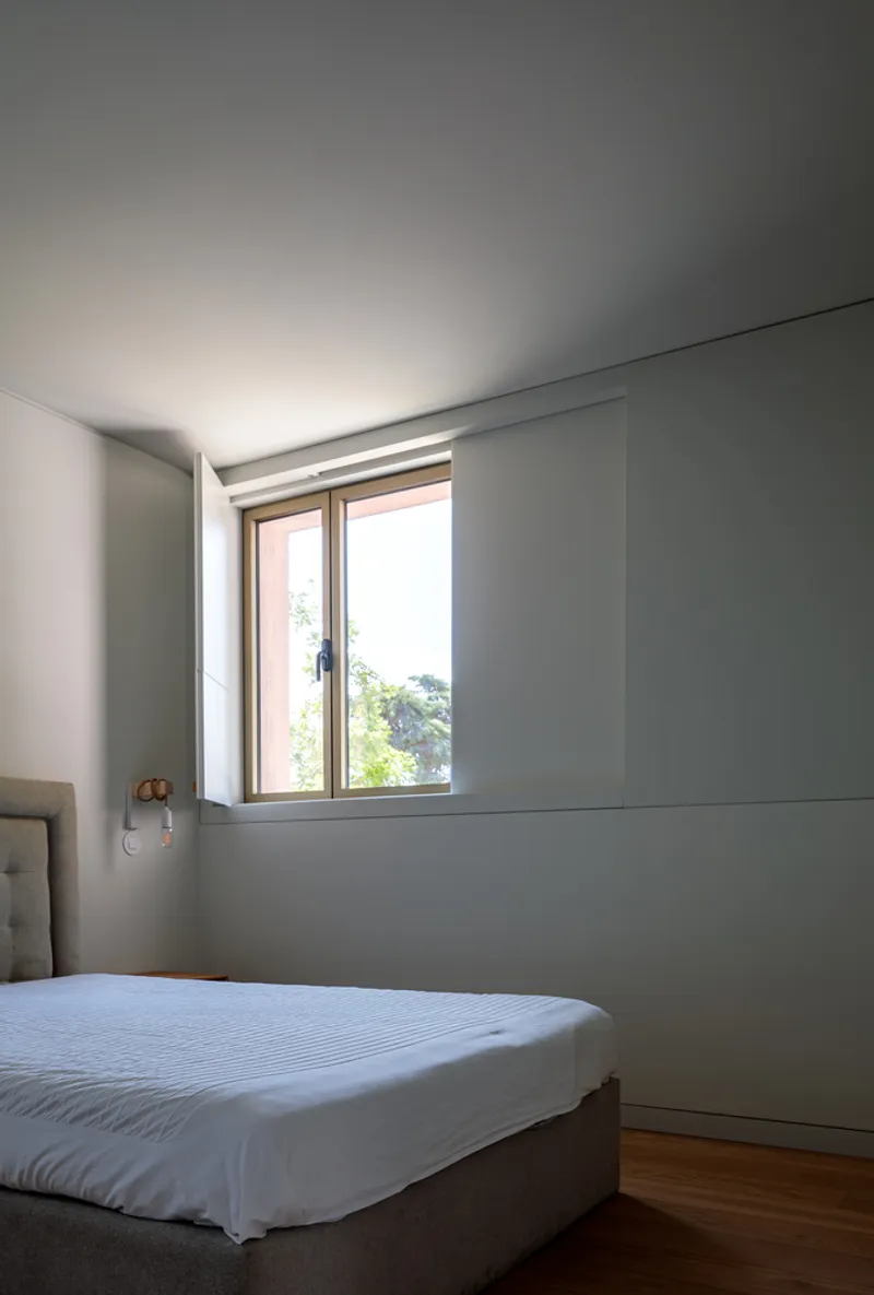 Bedroom with recessed window framed in timber revealing green foliage outside