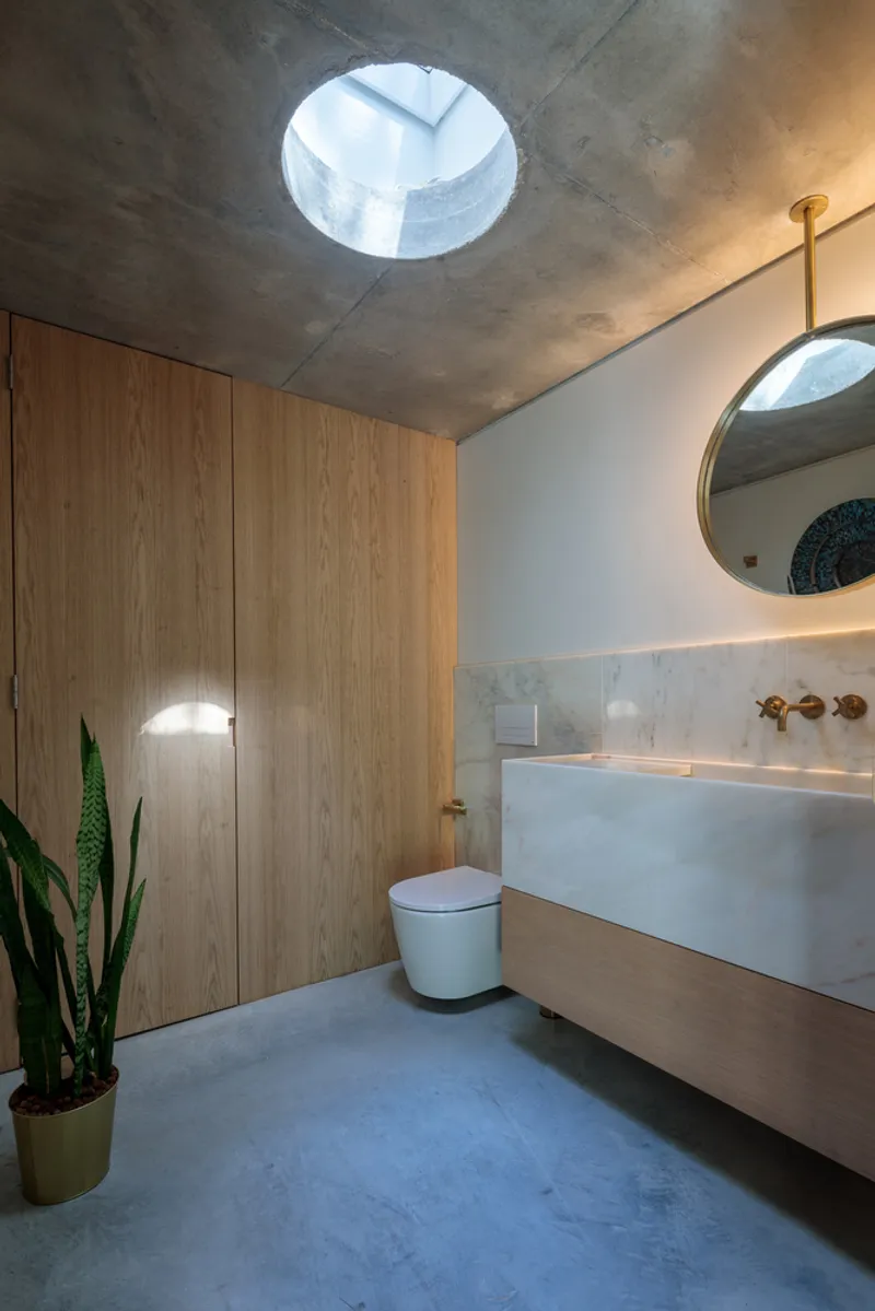 Bathroom with circular skylight above timber cabinetry and floating vanity under concrete ceiling
