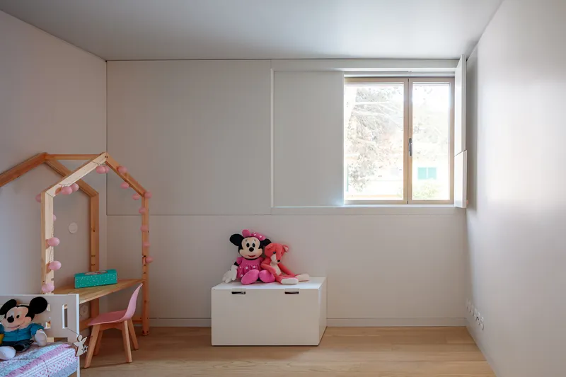 Children's bedroom with light oak flooring, built-in white storage, and window framing winter trees