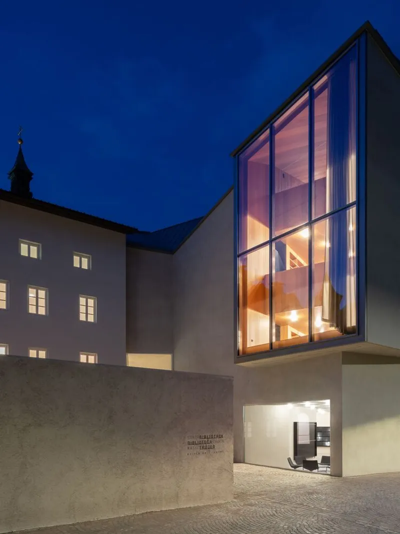Tall glazed stair volume adjoining a courtyard with historic building at blue hour