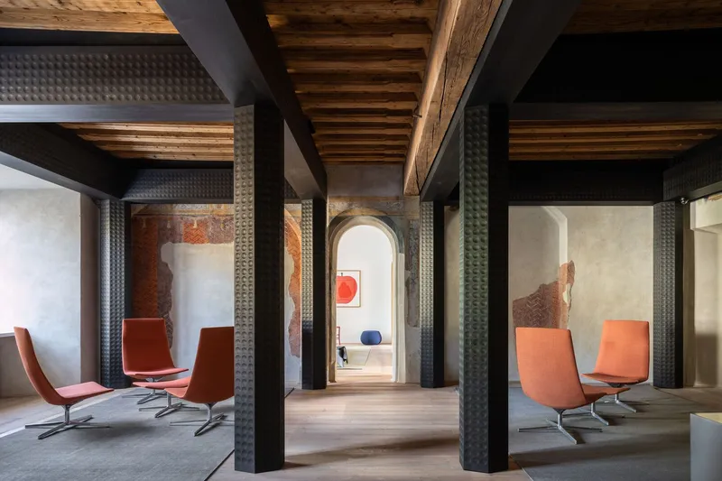 Gallery space with black textured columns supporting exposed timber beams and orange chairs