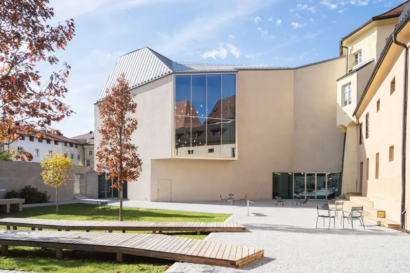 Courtyard view of the glazed facade with metal roof and timber deck platforms under blue sky