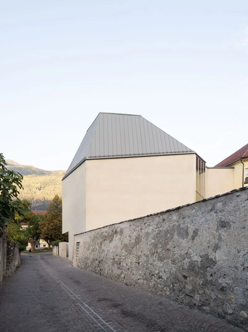 Street view of the blank stucco facade rising above the weathered stone wall at dusk