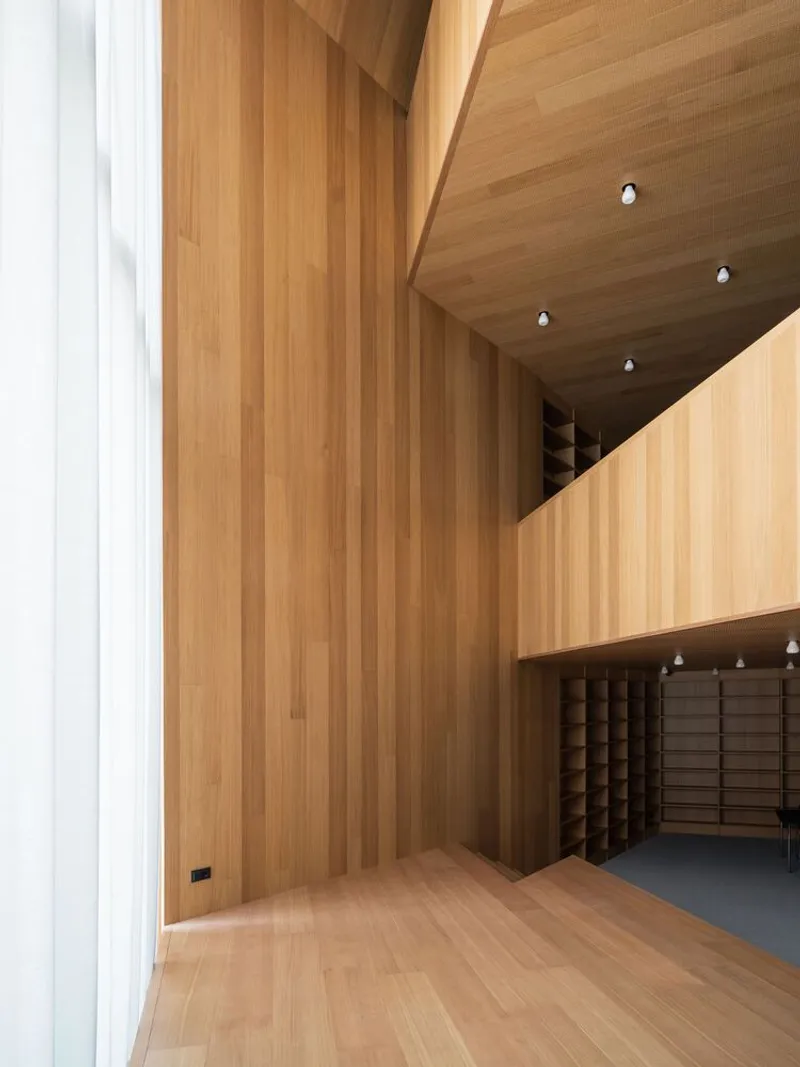 Double-height timber-clad interior space with vertical plank walls, shelving alcoves, and recessed ceiling lights
