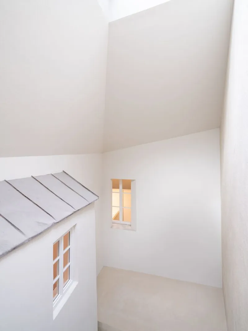 White play structure with miniature pitched roof and windows nestled within an enclosed white room