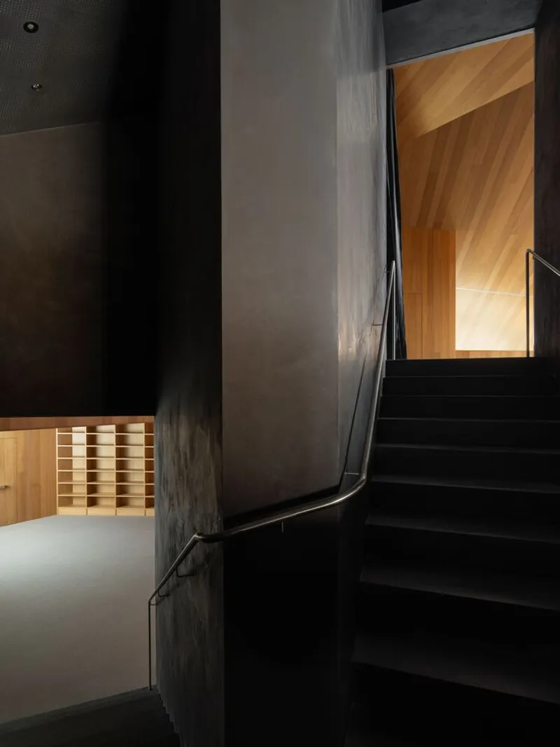 Black steel staircase winding between charcoal concrete walls and illuminated timber-clad doorways