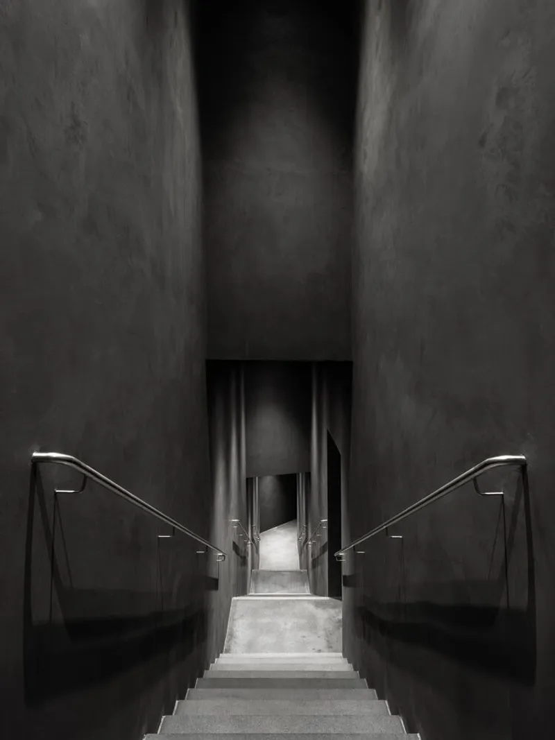 Symmetrical concrete stairwell descending between tall narrow walls toward a distant doorway