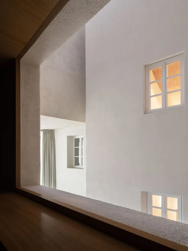 Interior courtyard view through a timber-framed opening showing white rendered walls with illuminated windows