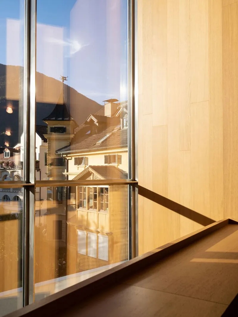 Corner glazing reflecting pitched roofs in afternoon sunlight with timber wall panels inside