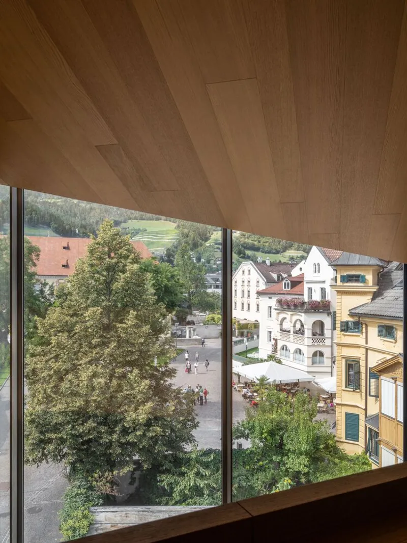 Window seat with timber ceiling panels framing views of the town square and hillside