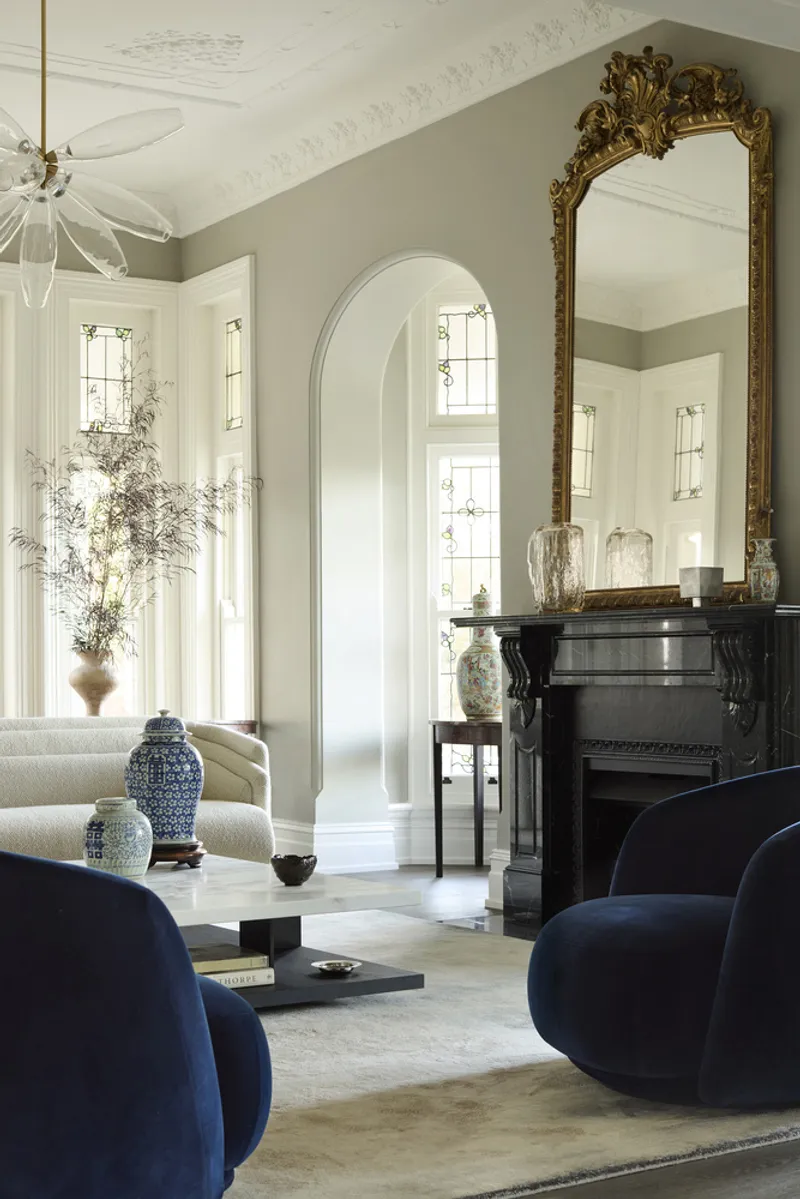 Living room with arched doorway, ornate mirror above black fireplace and afternoon light through leaded windows