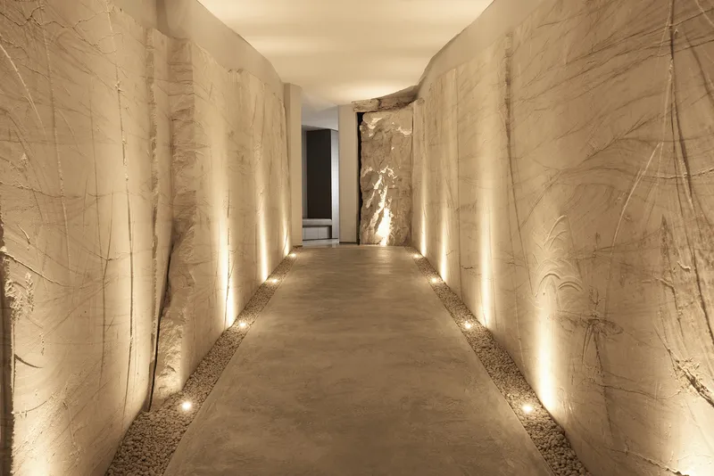 Corridor with carved limestone walls illuminated by floor-level lighting along both edges