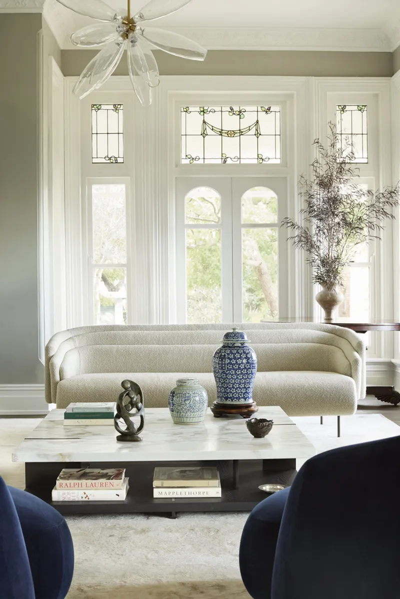 Living room with tall white-framed windows featuring decorative leadlight transoms and dappled afternoon light