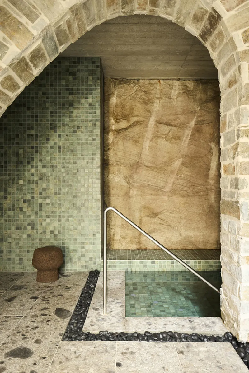 Vaulted stone grotto with mosaic tile plunge pool and sandstone feature wall beneath an arched ceiling