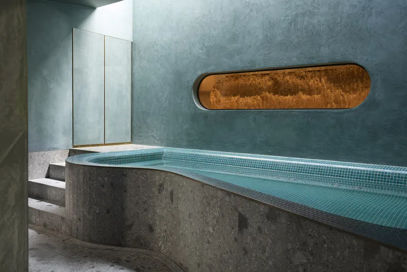 Curved concrete pool ledge with turquoise tile lining beneath an oval rusted metal window opening