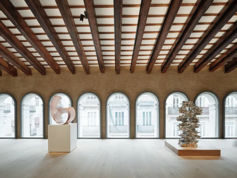 Gallery space with arched window openings and an exposed timber beam ceiling under natural daylight