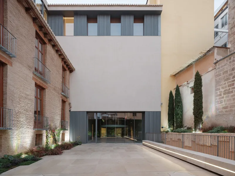 Courtyard entrance facade with vertical fluted metal panels and glass doors at twilight