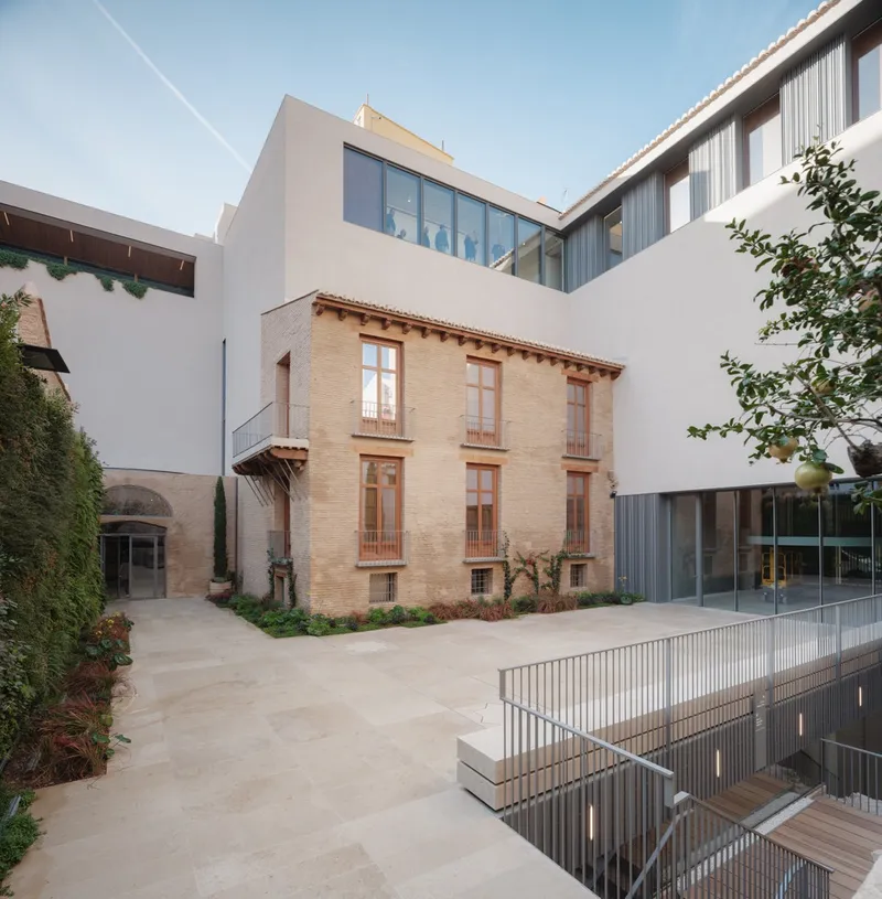 Interior courtyard showing preserved brick volume surrounded by whitewashed walls and glazed additions at dusk