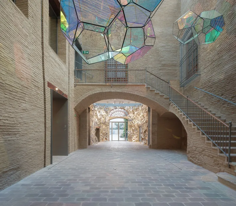 Vaulted entry hall with exposed brick staircase ascending beneath polyhedral stained glass skylight elements