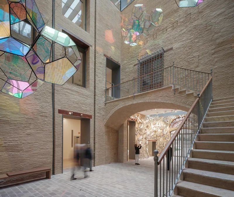 Multi-level atrium space with blurred visitor passing beneath arched stairway and textured wall relief