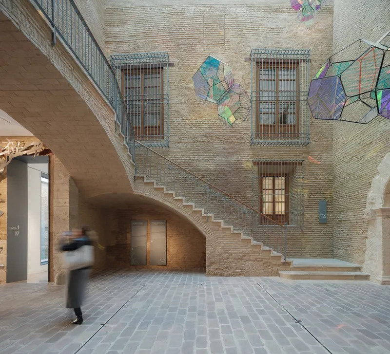 Brick courtyard lobby with visitor in motion crossing stone pavers below ascending staircase and colorful glass installations