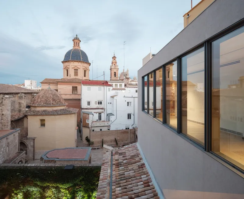 Rooftop terrace with glazed facade overlooking terra-cotta roofs and church domes at dusk
