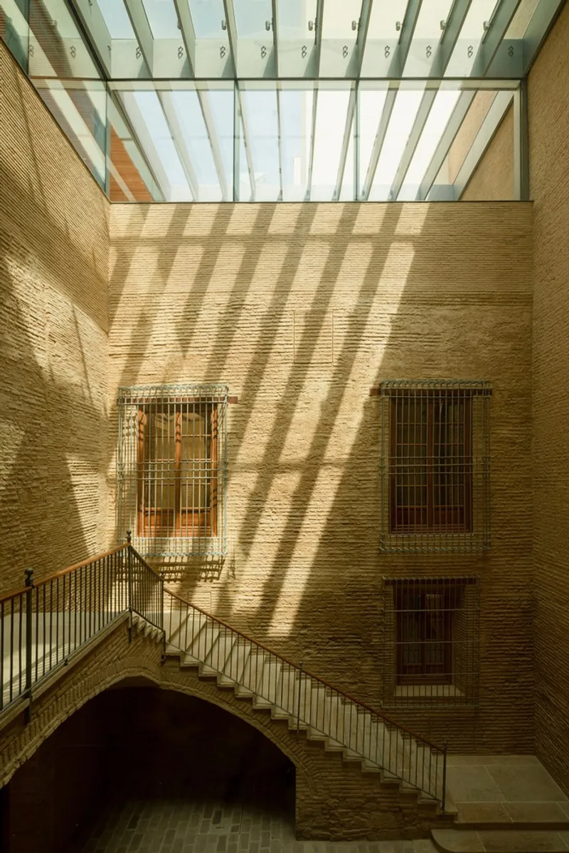 Brick courtyard with metal stair and glazed skylight casting striped shadows across the wall