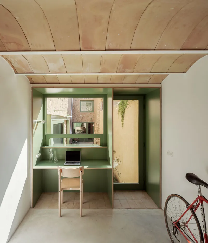 Built-in desk alcove with green painted shelving beneath a curved plywood ceiling and bicycle parked alongside