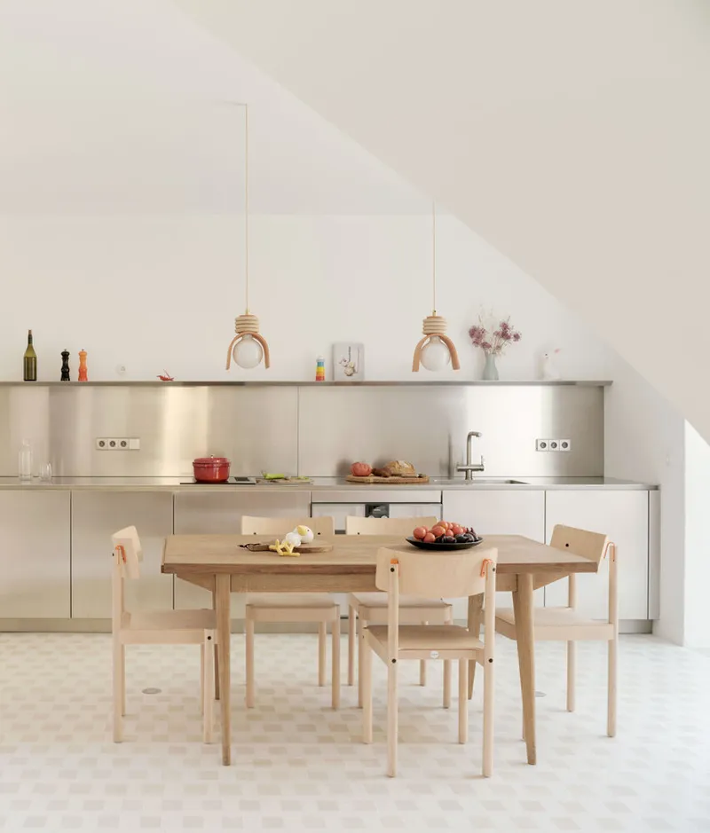 Kitchen and dining area with stainless steel backsplash and timber furniture under a sloped white ceiling