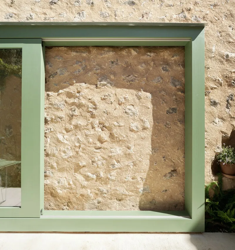 Green metal window frame revealing layers of weathered plaster on the stone wall behind