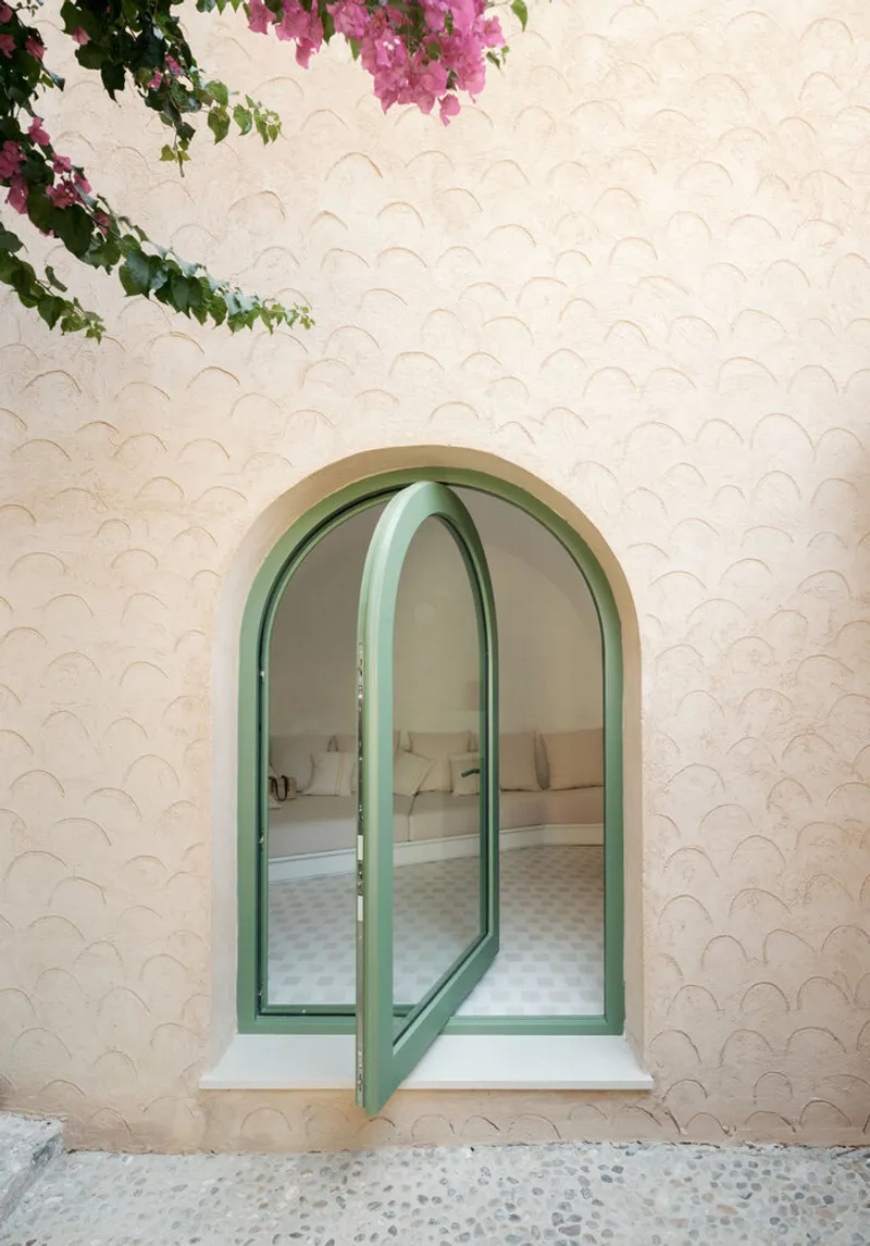 Arched green window with scale-patterned white facade and pink bougainvillea overhead