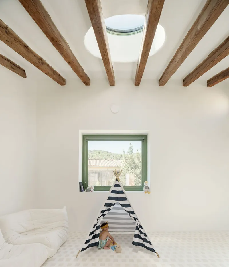 White room with exposed timber ceiling beams and circular skylight above a child's play tent