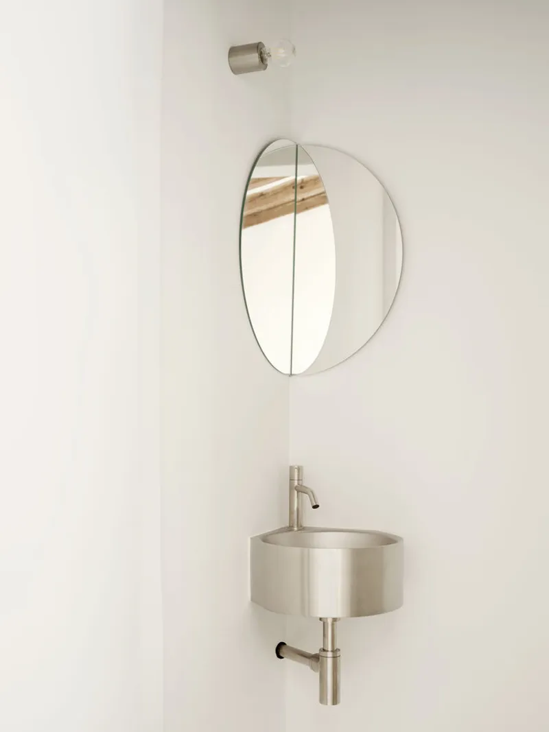 Wall-mounted round basin with brass fixtures and oval mirror