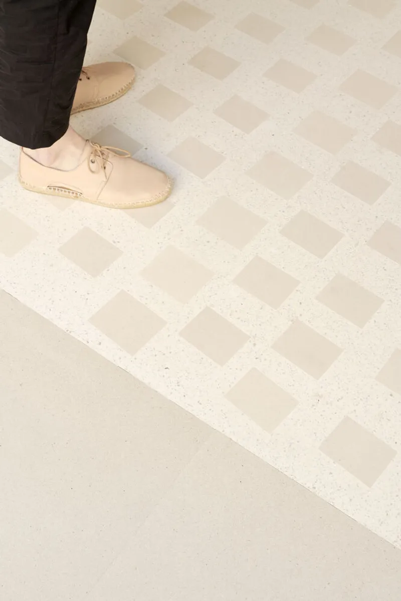 Terrazzo floor with alternating checkerboard pattern of smooth and textured cream tiles as a visitor walks across